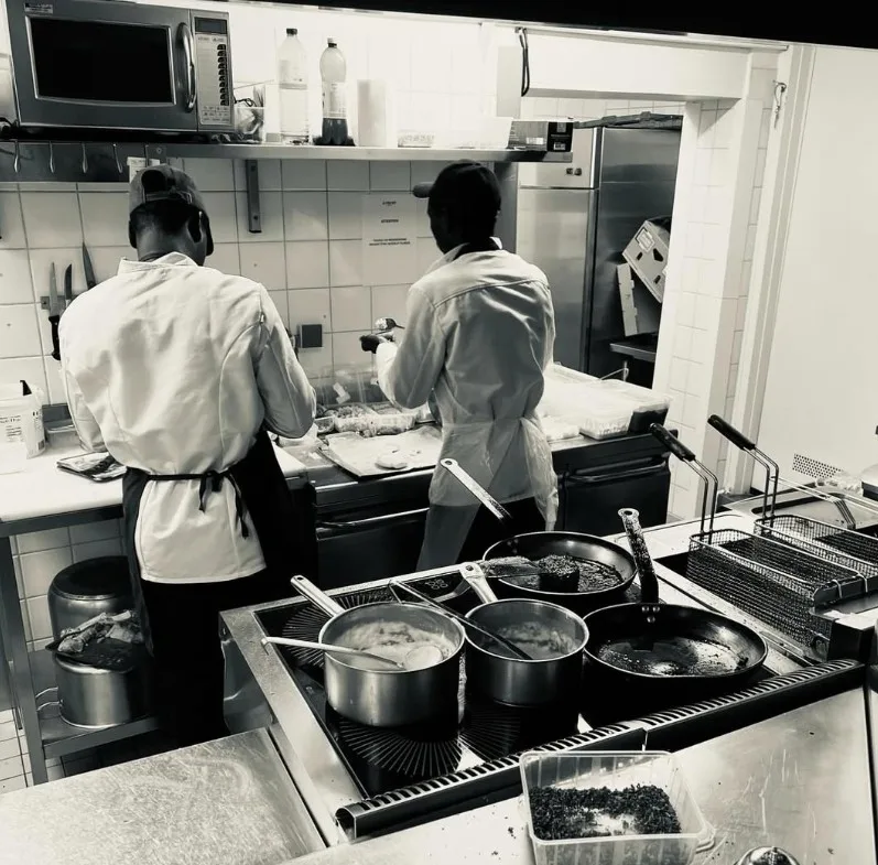Deux cuisiniers d'August en plein service dans la cuisine du restaurant (photo en noir et blanc).