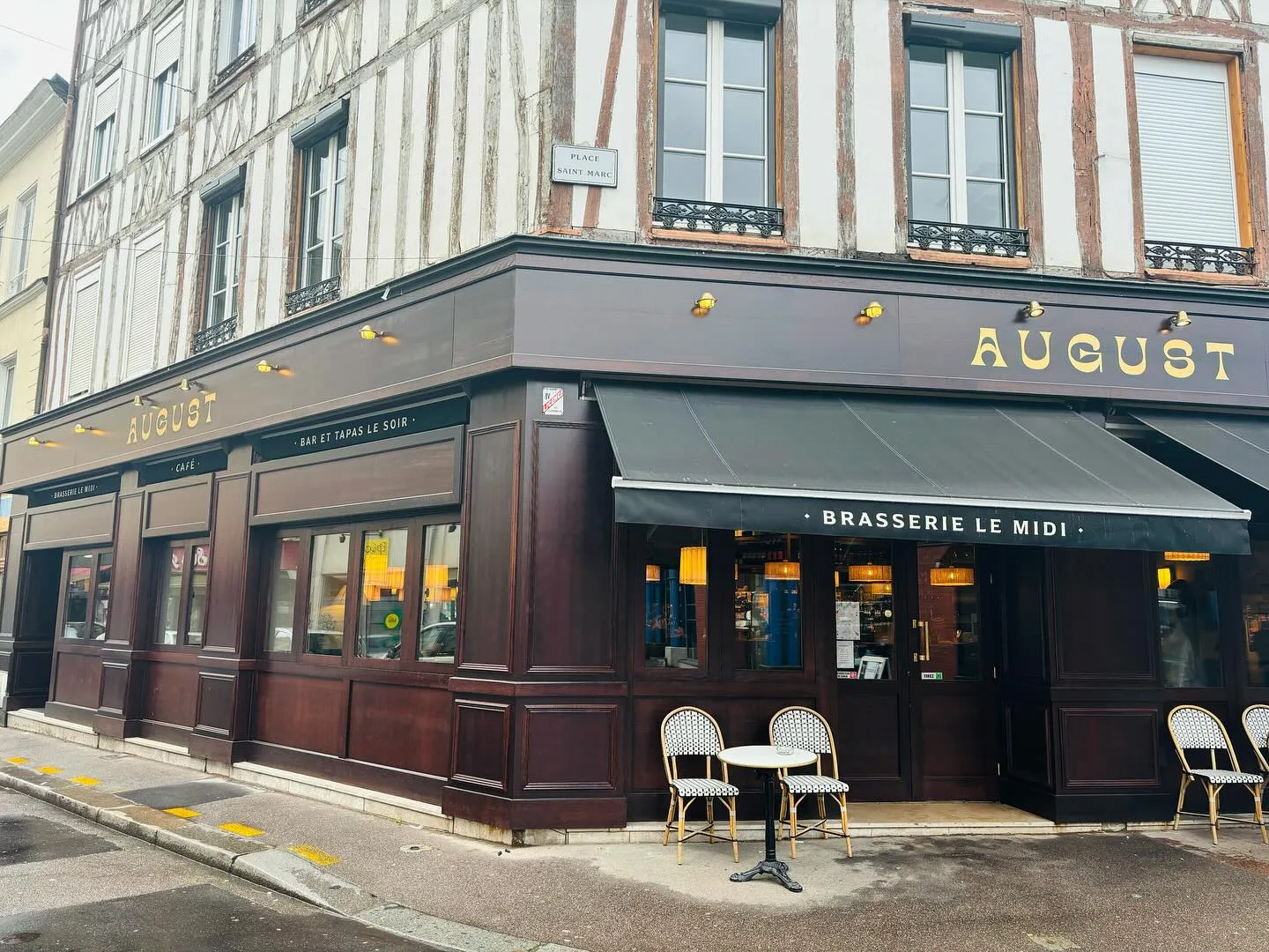Façade d'August à l'angle de la place Saint-Marc à Rouen, devanture en bois sombre, enseigne dorée et terrasse en bordure de trottoir.