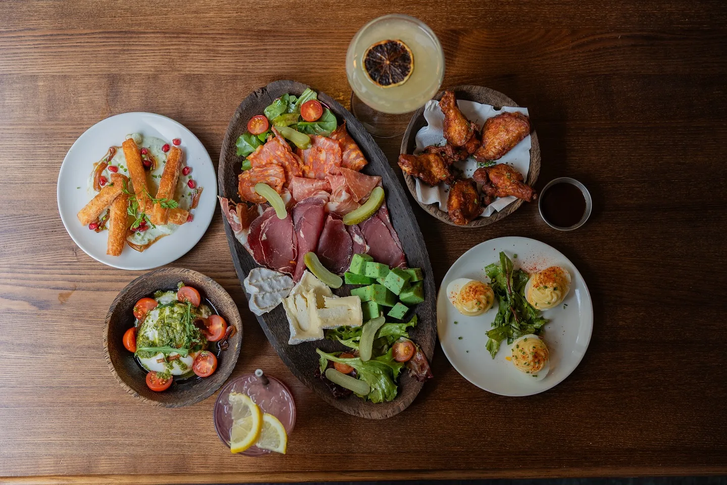 Assortiment de tapas et planches à partager chez August : charcuterie, fromages, ailes de poulet, burrata et œufs garnis, accompagnés de cocktails.