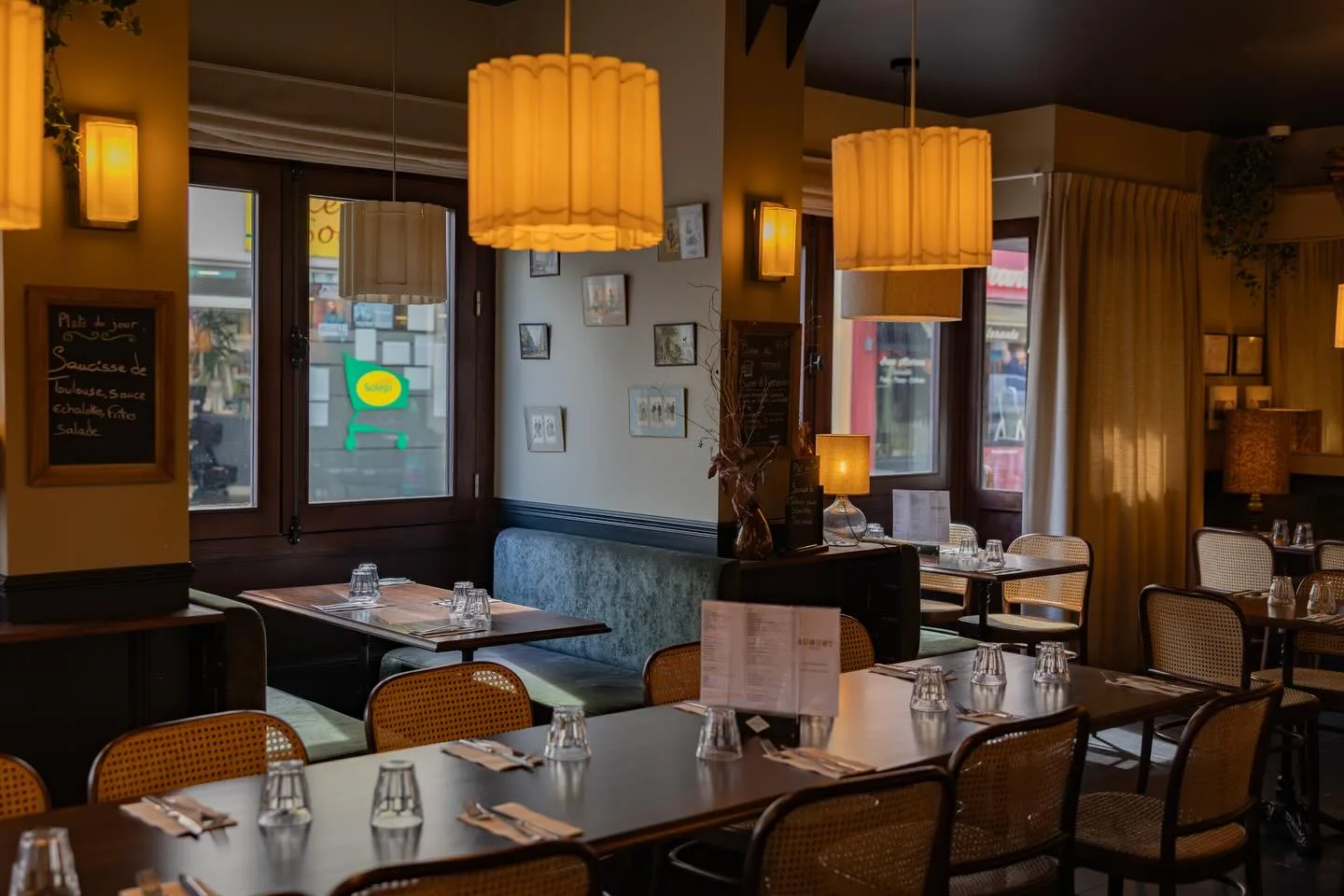 Salle d'August à Rouen : tables dressées, chaises bistrot cannées, banquette en velours et suspensions Art déco.