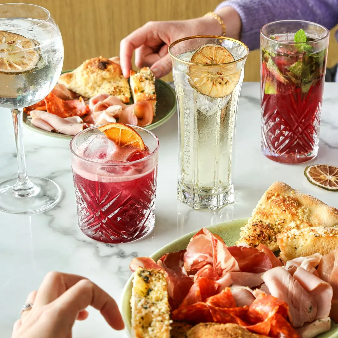 Table en marbre du Del Arte Isneauville avec planche d'antipasti italiens (jambon de Parme, coppa, focaccia et grissini) accompagnée de cocktails et boissons signatures