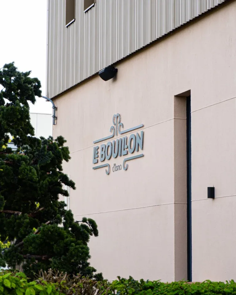 Façade beige du restaurant Le bouillon d'Isno à Isneauville avec le logo apposé sur le mur et un arbre vert en premier plan.
