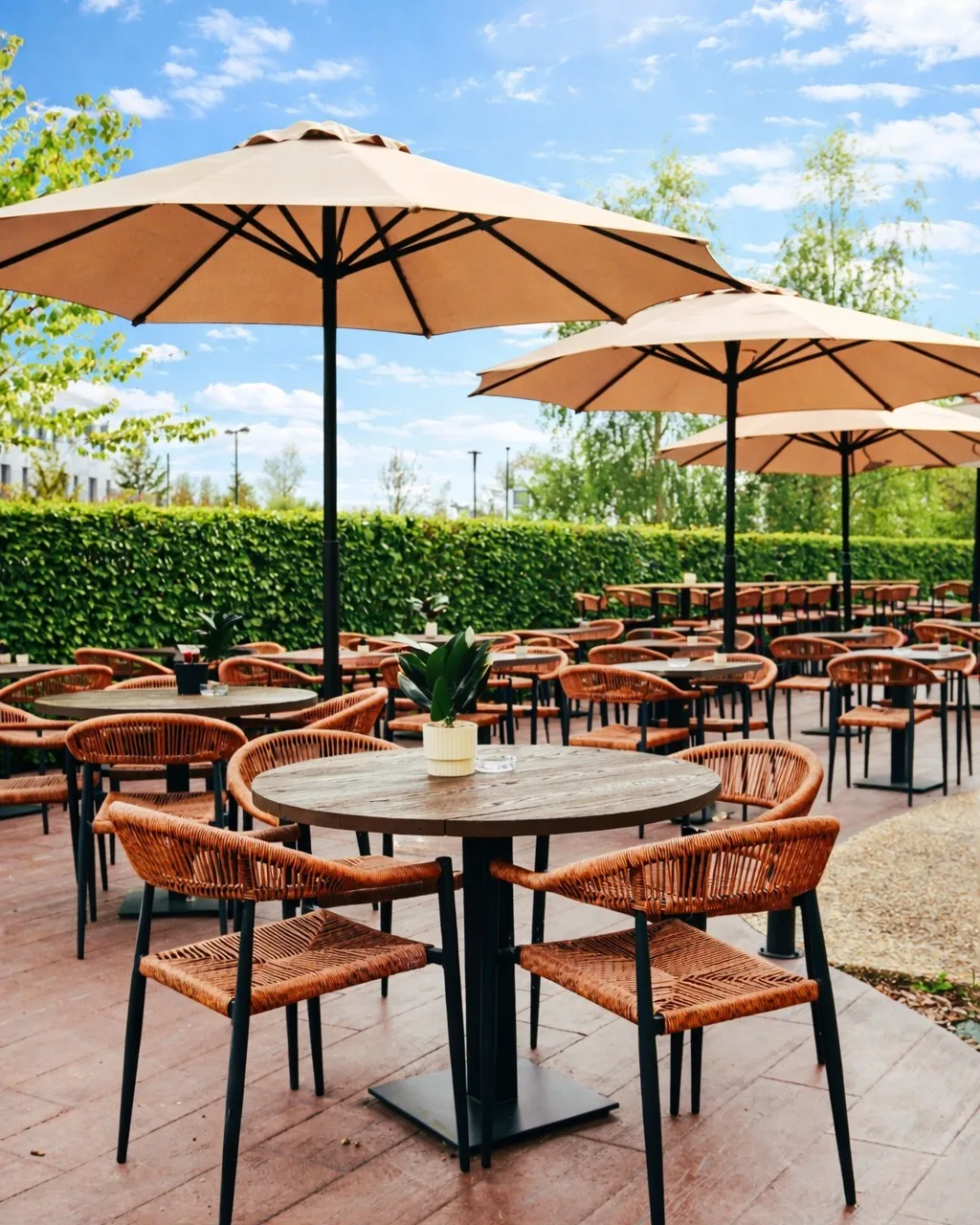 Terrasse extérieure ensoleillée du Bouillon d'Isno avec parasols beiges, tables rondes en bois et chaises tressées orange devant une haie verte.