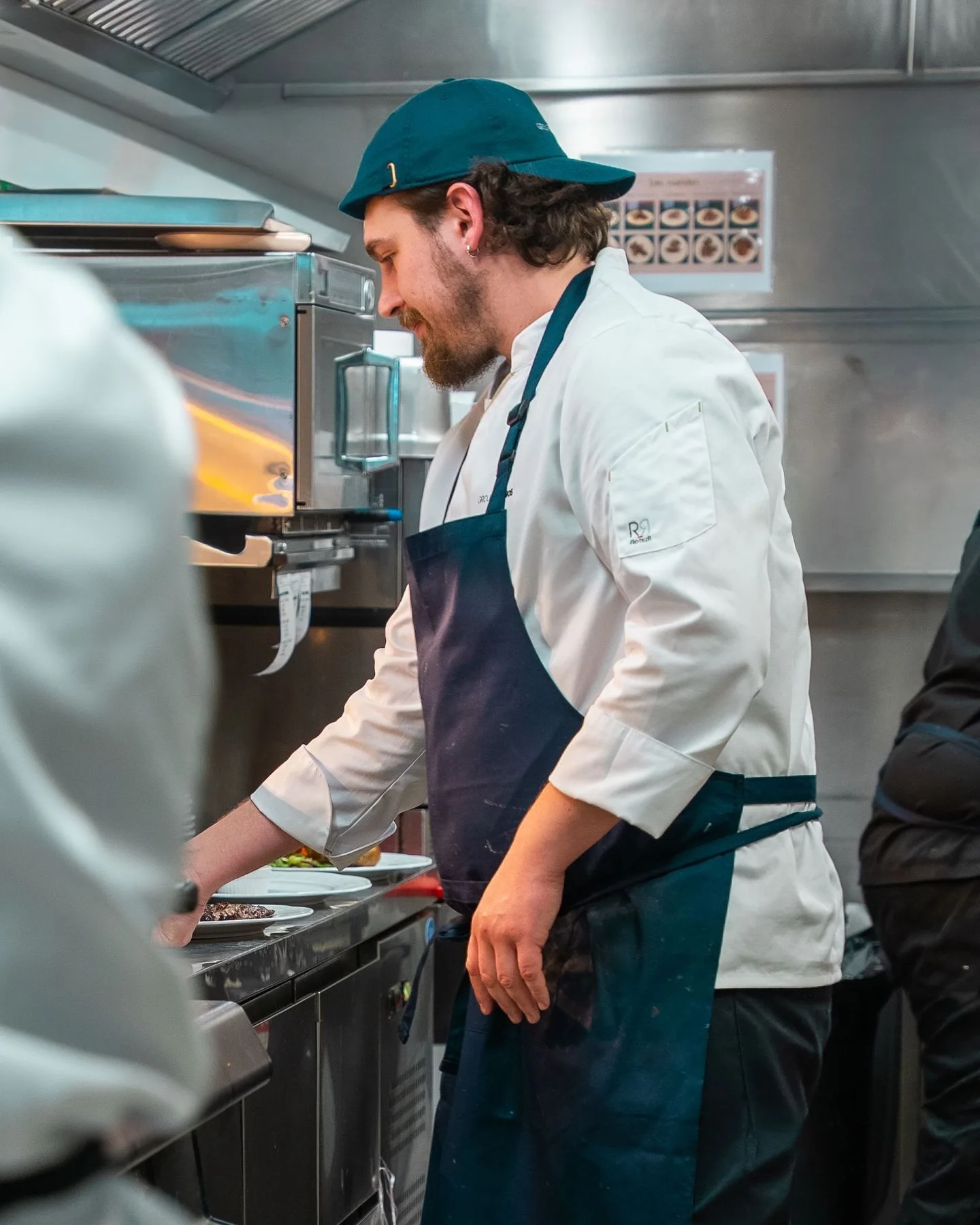 Cuisinier de l'équipe Mimosa en cuisine, veste blanche et tablier bleu, dressant les assiettes