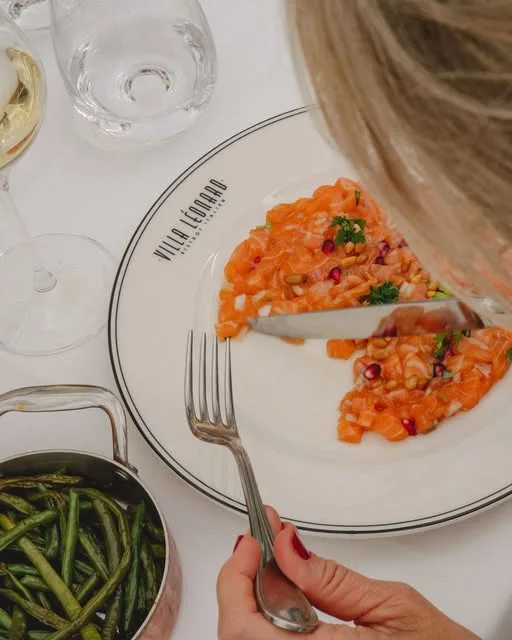 Tartare de saumon, grenade, mangue et basilic, servi sur l'assiette siglée Villa Léonard avec des haricots verts