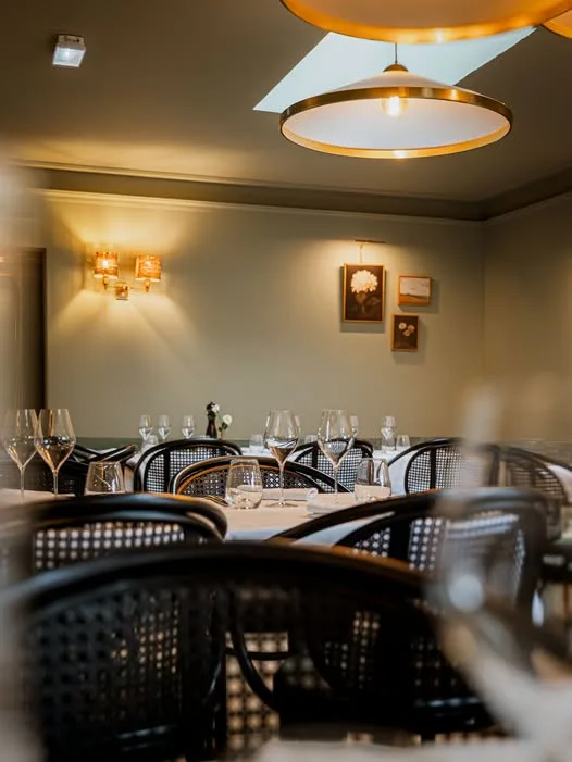 Salle de restaurant de la Villa Léonard : murs olive, chaises cannées et grandes suspensions dorées