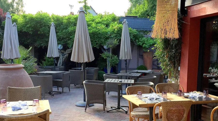 Terrasse extérieure de la Villa Léonard : tables en rotin, parasols et végétation, le long du mur du restaurant